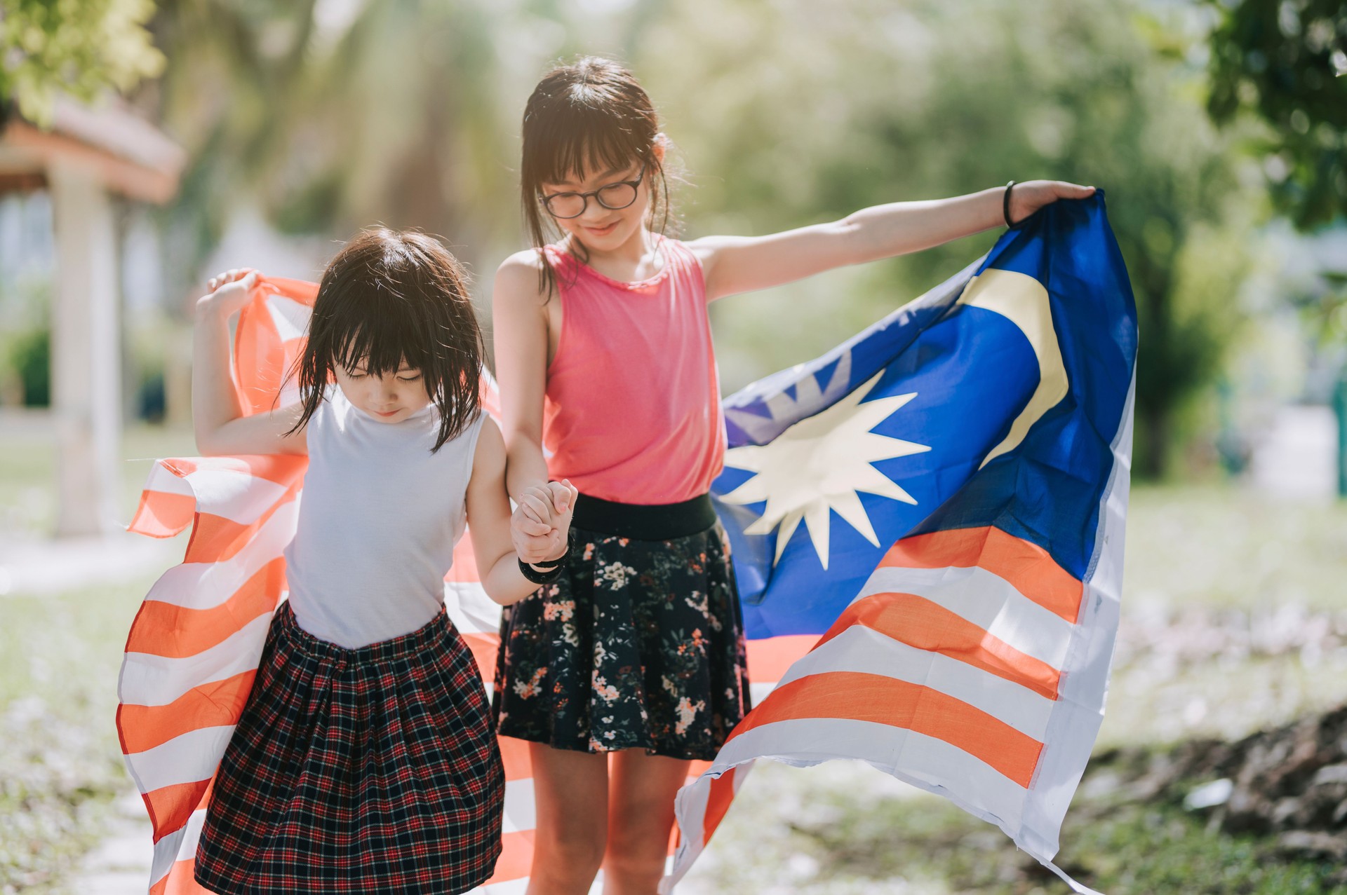 2 asian chinese young girl playing and spending bonding time in public park wrapping with malaysia national flag